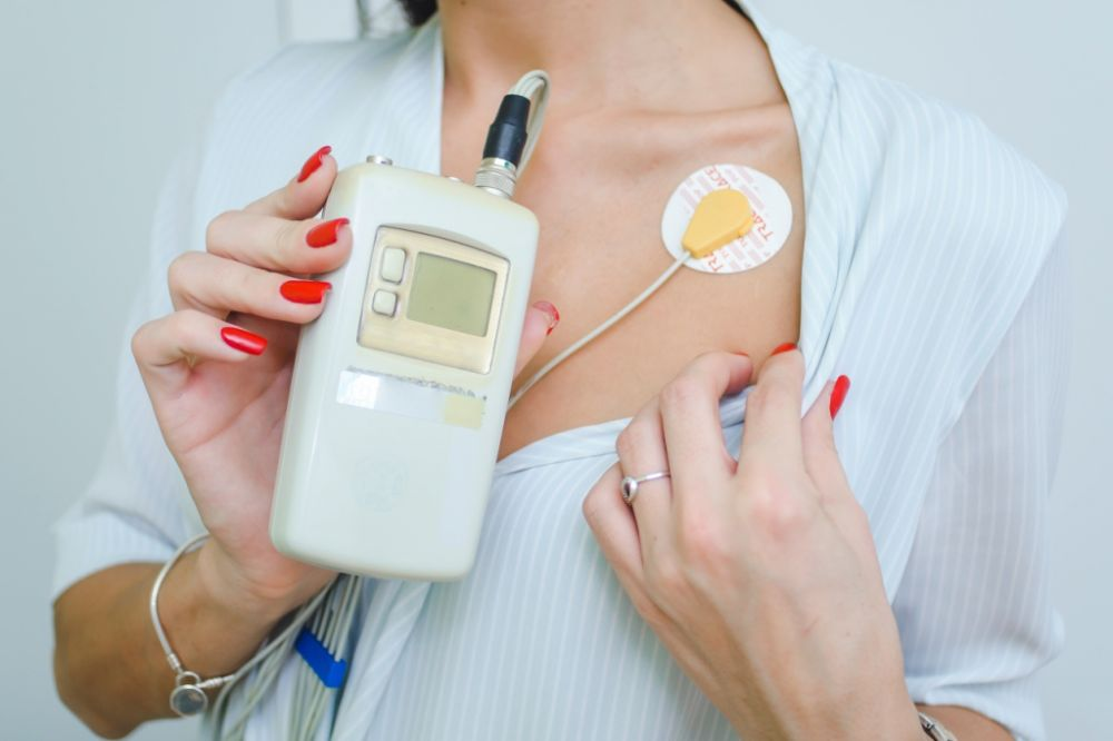 A woman holds a portable medical device connected to a patch on her chest.